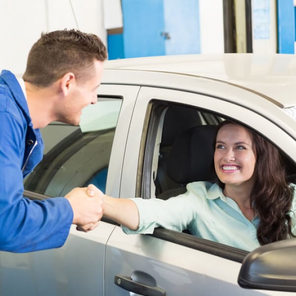 Woman in passenger seat of car shaking the hand of a service person standing outside of the car.