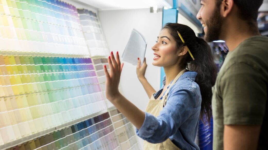 Female paint store employee assisting a male customer, showing him different paint swatches